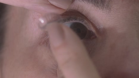 close-up of a person's eye with a finger adjusting a contact lens or prosthetic