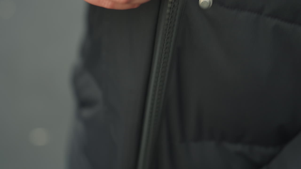 Closeup of caucasian womans hands fastening jacket zipper, lower torso view, subtle rhythmic pull, beanie visible, lining glimpse, cold outdoor pavement, precise finger movement, routine moment