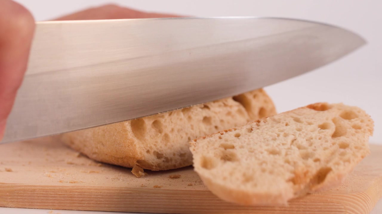 Chef slices crusty sourdough bread on a wooden board using a sharp kitchen knife.