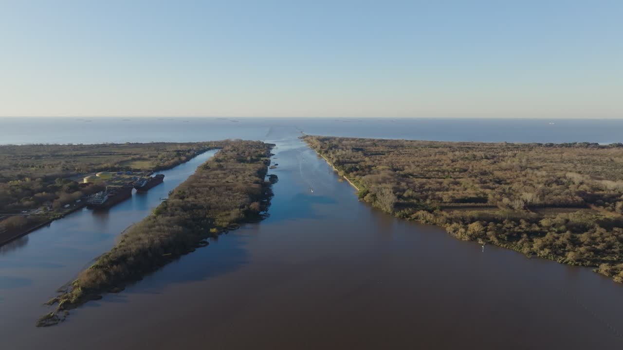 Daytime drone footage showing a cargo vessel at a busy river port with docks, containers, and industrial activity