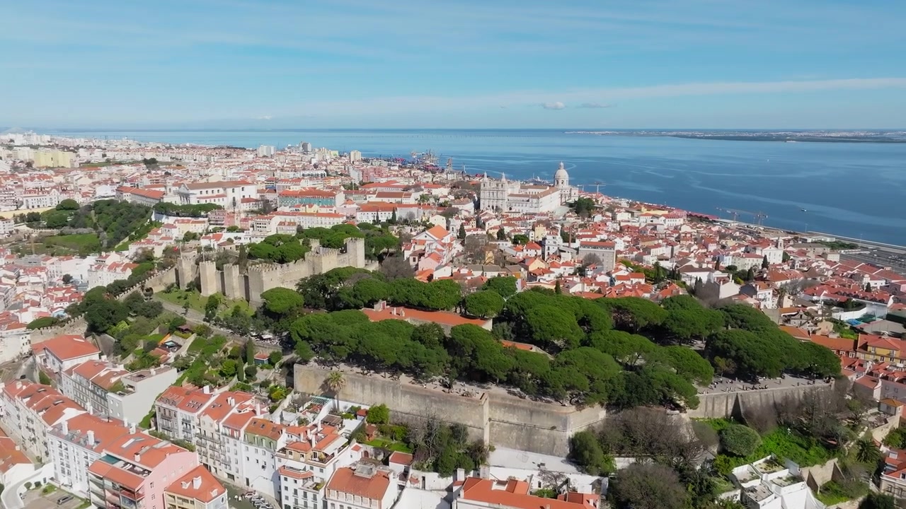 Lenta ripresa panoramica con drone del Castello di São Jorge, Lisbona a mezzogiorno. Il Pantheon Nazionale visibile dietro. Cielo azzurro limpido, sole splendente. Portogallo.