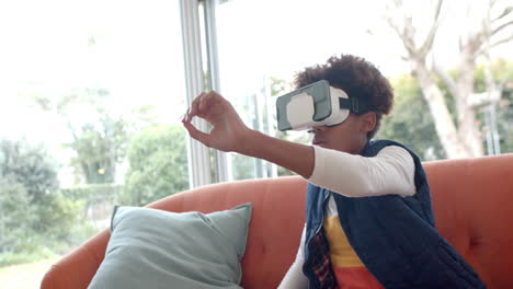 African-american-boy-sitting-on-sofa,-using-vr-headset-and-touching-virtual-screen,-slow-motion