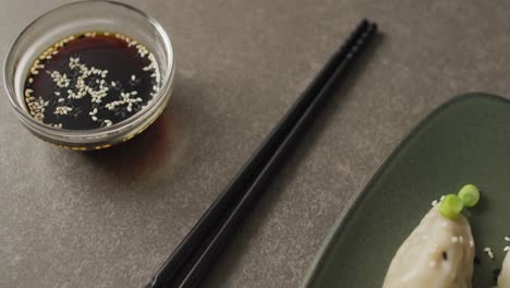 Composition-of-plate-with-gyoza-dumplings-and-soy-sauce-with-chopsticks-on-grey-background