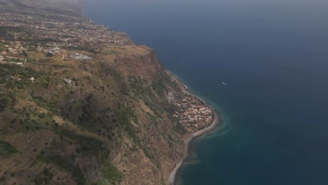 Vista-Aérea-De-La-Parroquia-De-Calheta-En-La-Isla-De-Madeira,-Sobrevolando-La-Costa-Mostrando-El-Contraste-Entre-El-Pueblo-Junto-Al-Mar-Y-El-Resto-De-Las-Casas-En-Lo-Alto-De-La-Montaña