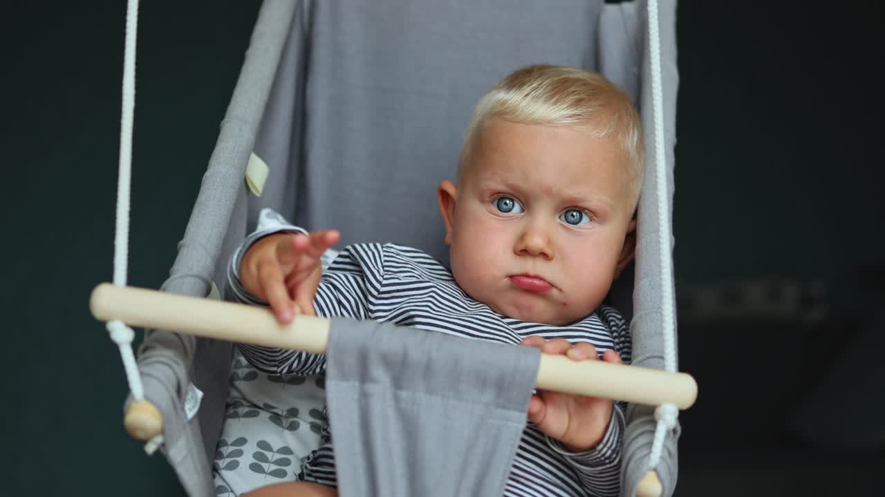 A Playful Baby in a Cozy Hanging Swing While Showcasing Strikingly Beautiful Blue Eyes