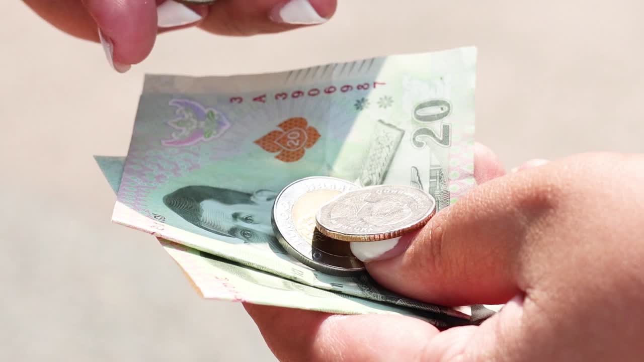 Detailed view of hands handling banknotes and coins in an outdoor setting.
