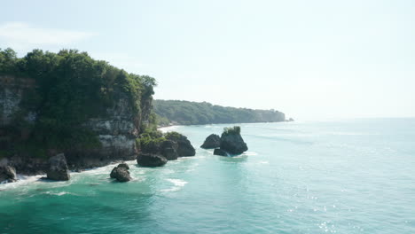 Tiro-Aéreo-Bajo-Volando-Por-Acantilados-Oceánicos-Escarpados-Sobre-El-Mar-Azul-Turquesa-Tropical-En-Bali,-Indonesia