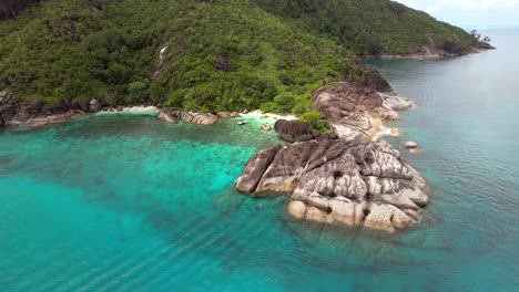 Drone-shot-rotate-bear-secluded-rice-beaches,-docked-boat-with-clients,-lush-national-park-and-turquoise-ocean,-Mahe-Seychelles-30-fps
