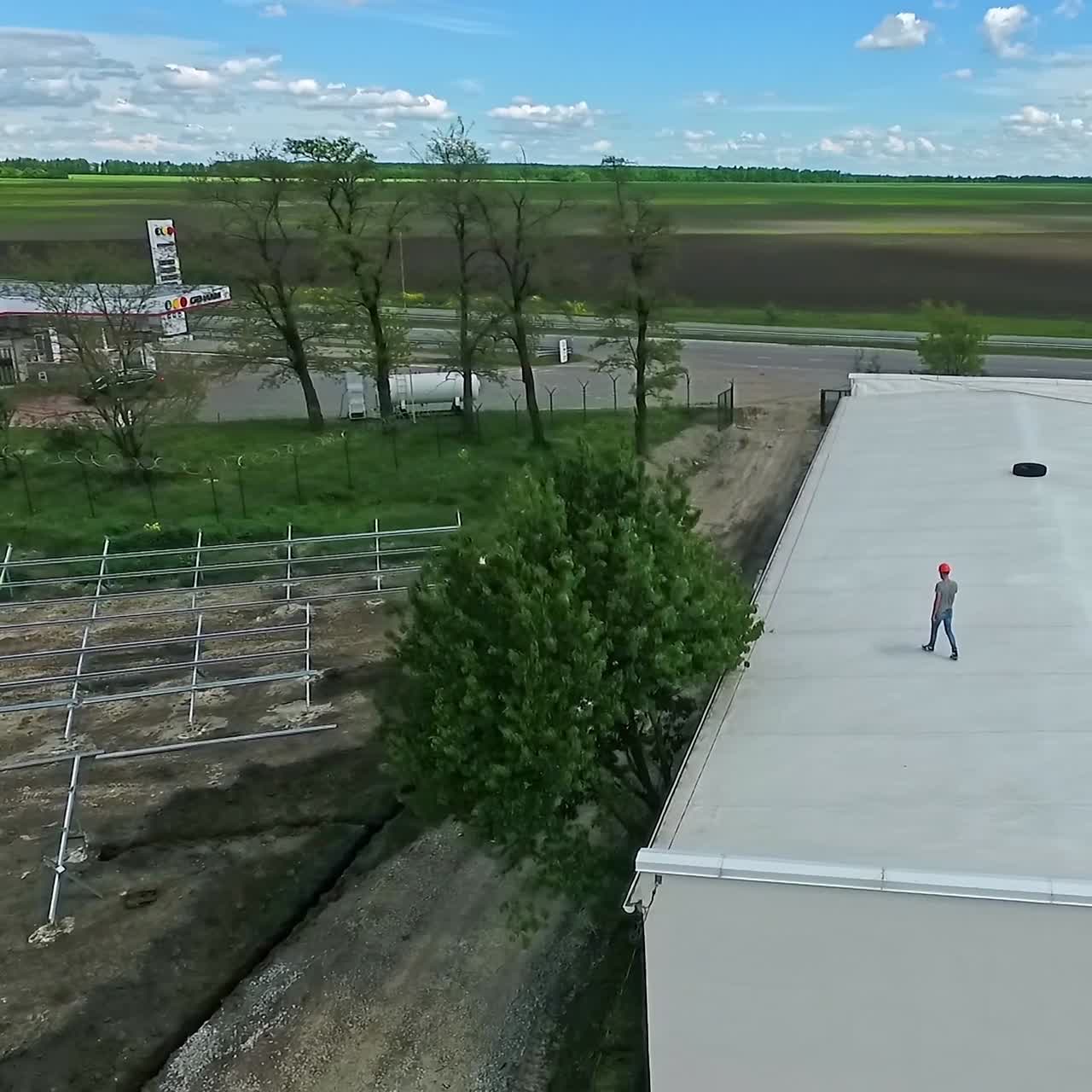 Engineer expert walking on roof. Worker in orange helmet think about new solar farm construction on rooftop of a building on nature background. Aerial view. Motion camera around.