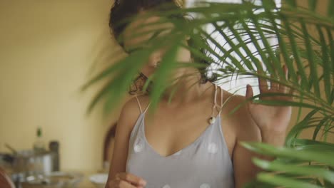 una joven hermosa con cabello rizado posando para una cámara junto al elegante concepto de disparo interior de chamaedorea