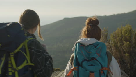 back view of two female hikers reaching the mountain top, then hugging, raising hands and enjoying the view