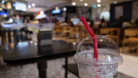 Roter-Strohhalm-In-Einem-Plastik-Einwegbecher-Auf-Einem-Food-Court,-Während-Sich-Menschen-Im-Hintergrund-In-Bangkok-Bewegen