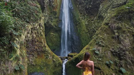 a woman stands in awe before the majestic vuelta al cañón waterfall in costa rica, surrounded by lush jungle and mist rising from the cascading water