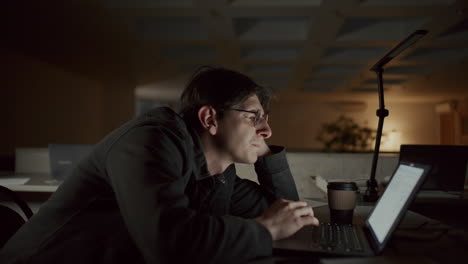 young man reading text on laptop as working overtime in office at night