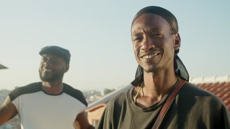 front view of happy gays in bandana and cap looking at camera on rooftop