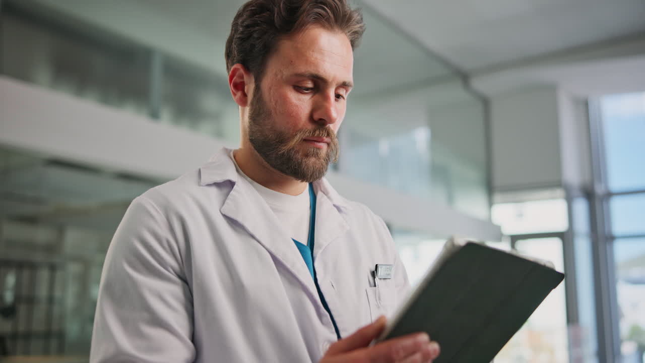 Medico uomo concentrato in camice da laboratorio che usa un tablet digitale.