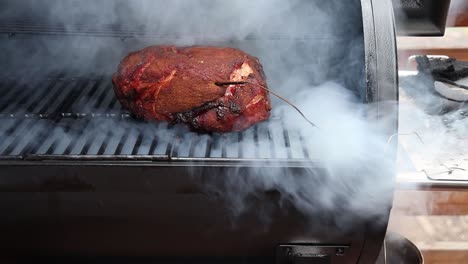 abrir la tapa de un fumador para revelar humo pesado y un trasero de cerdo antes de cerrar la tapa de nuevo