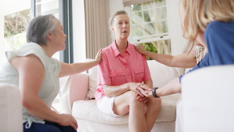 senior biracial woman receives comfort from two caucasian women at home