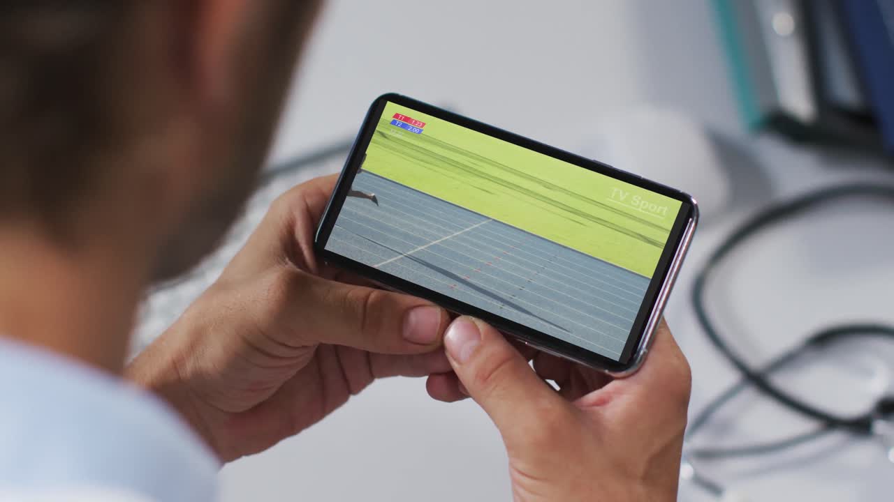 compuesto de un médico masculino viendo un evento de atletismo en un teléfono inteligente