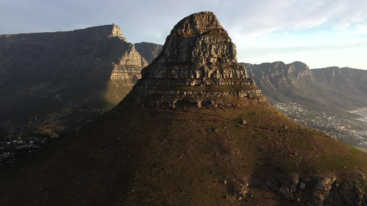 dramática toma cinematográfica sobrevolando el pico de la cabeza de león con la montaña de la mesa durante la puesta de sol de la hora dorada