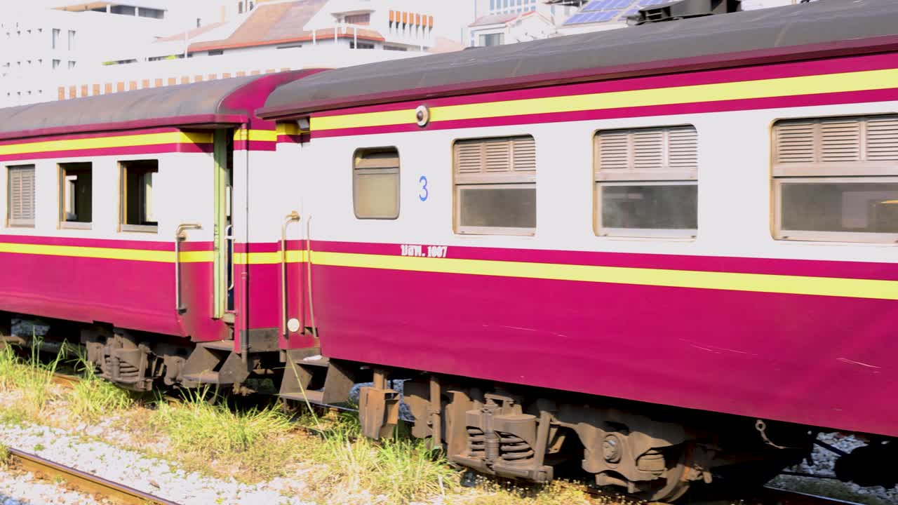 Un treno passeggeri magenta e giallo percorre i binari sotto la luce del giorno a Bangkok