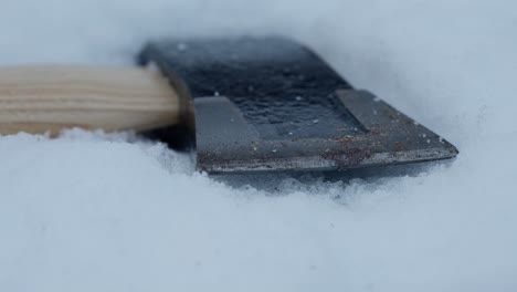 slow tracking shot along head of axe lying in soft snow, close up