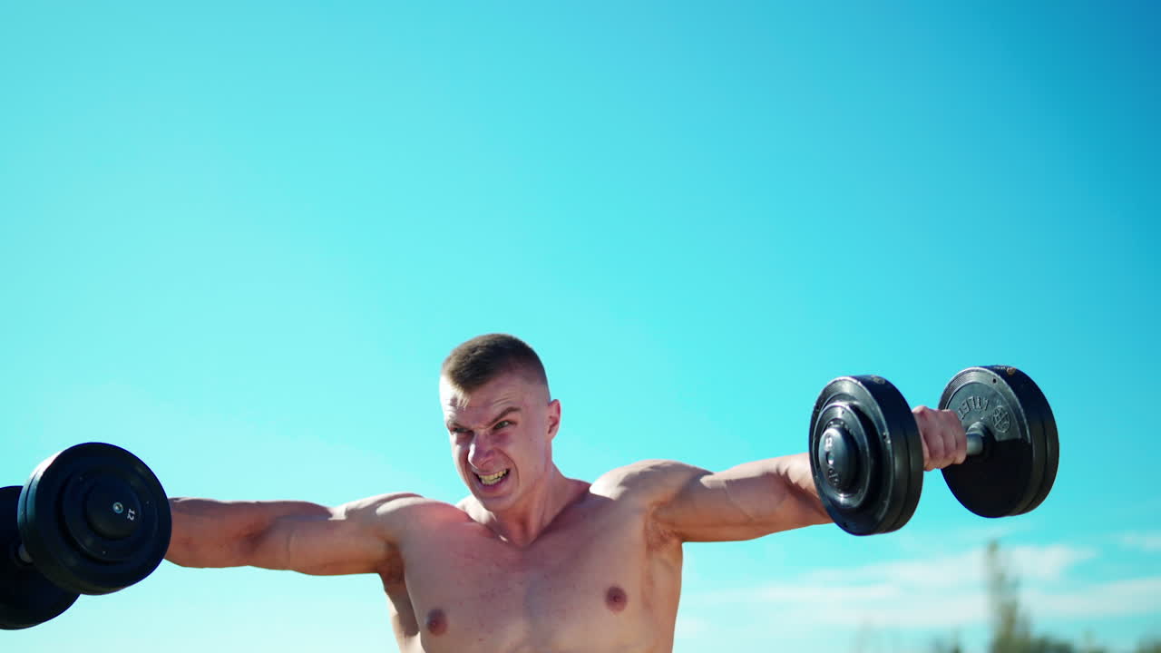 Workout fitness sport. Geconcentreerde jonge sporter traint buiten zijn bovenarmen met dumbbells.