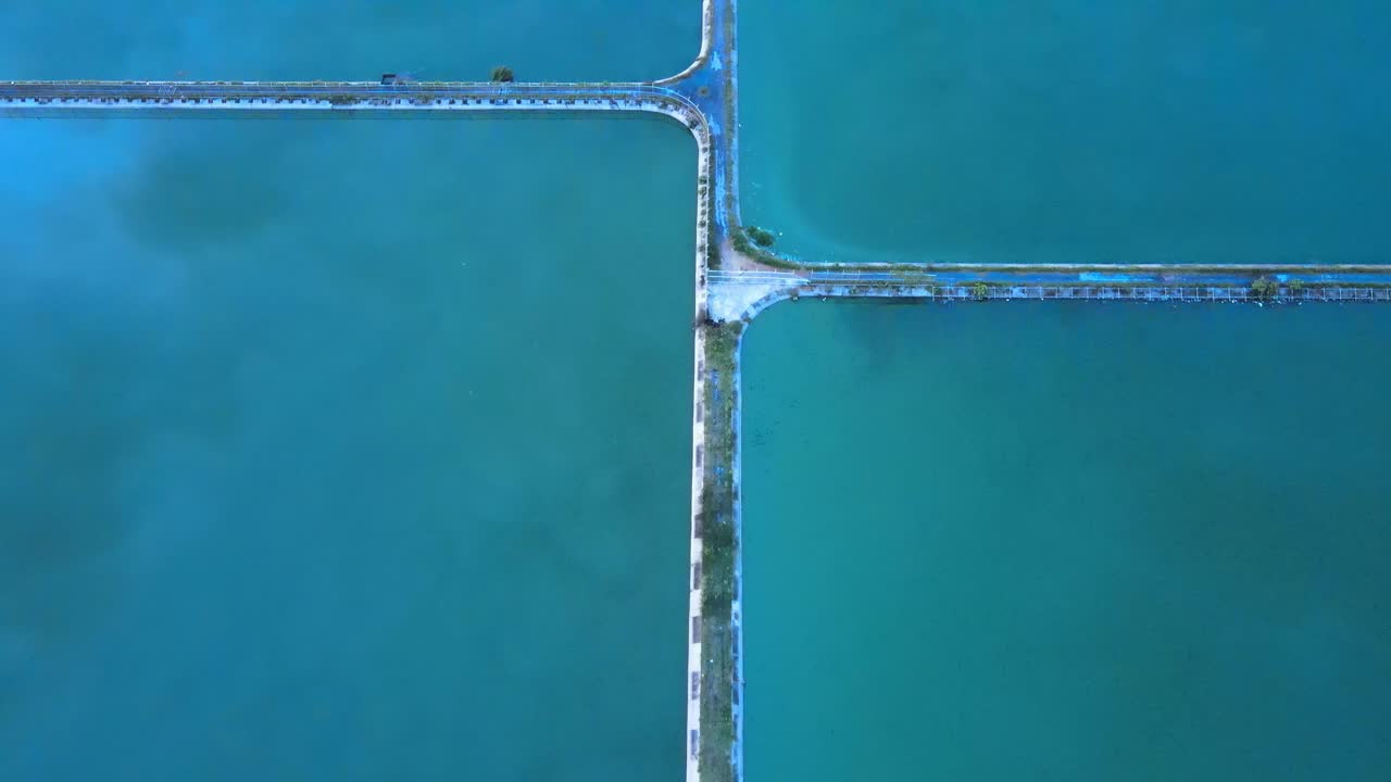 표면에 하늘을 반사하는 양어장 호수 위의 도로를 따라가는 공중 영상