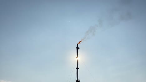 Gas-burns-in-a-chimney,-emitting-black-smoke-into-a-sunny-blue-sky