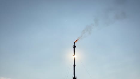 el gas se quema en una chimenea, emitiendo humo negro en un cielo azul soleado