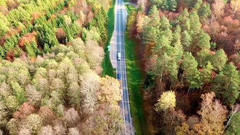 Vista-Aérea-De-Un-Coche-Conduciendo-Por-Una-Carretera-En-Un-Colorido-Bosque-Otoñal