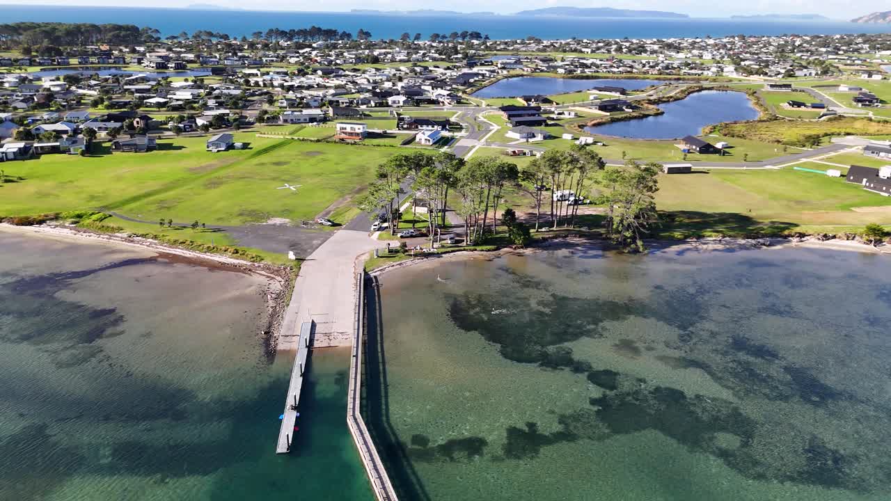 A 4K drone captures the stunning lake and beach at Matarangi Freedom Camp in New Zealand. Calm waters, sandy shores, and lush surroundings create a peaceful and scenic landscape