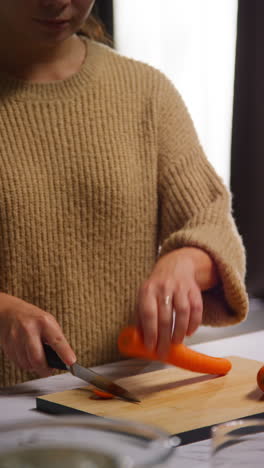 vertical video close up of woman at home in kitchen preparing healthy fresh vegetables for vegetarian or vegan meal chopping carrots on board 1