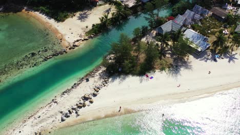 peaceful shoreline with turquoise lagoon entering into white sandy beach surrounded by palm trees and resort cabins in thailand