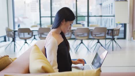 Video-of-asian-businesswoman-using-laptop-in-lounge-area-of-busy-office