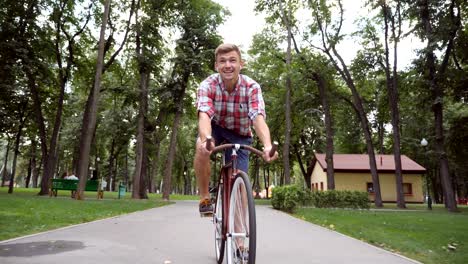 young happy man riding a vintage bicycle at park road and listening music. portrait of sporty guy cycling outdoor and sing song. healthy active lifestyle. front view close up slow motion