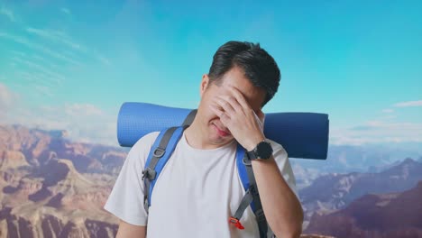 close up of asian male hiker with mountaineering backpack having a headache while traveling at the top of mountain
