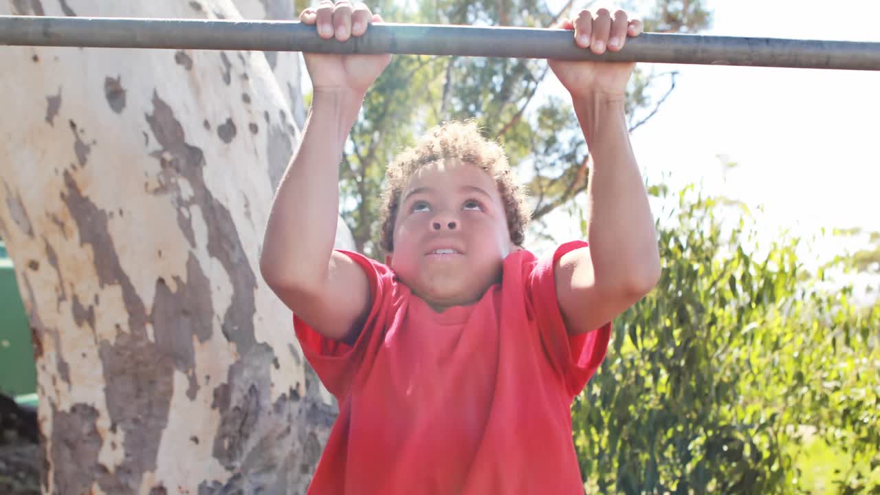 niño realizando pull-ups en la barra durante una carrera de obstáculos