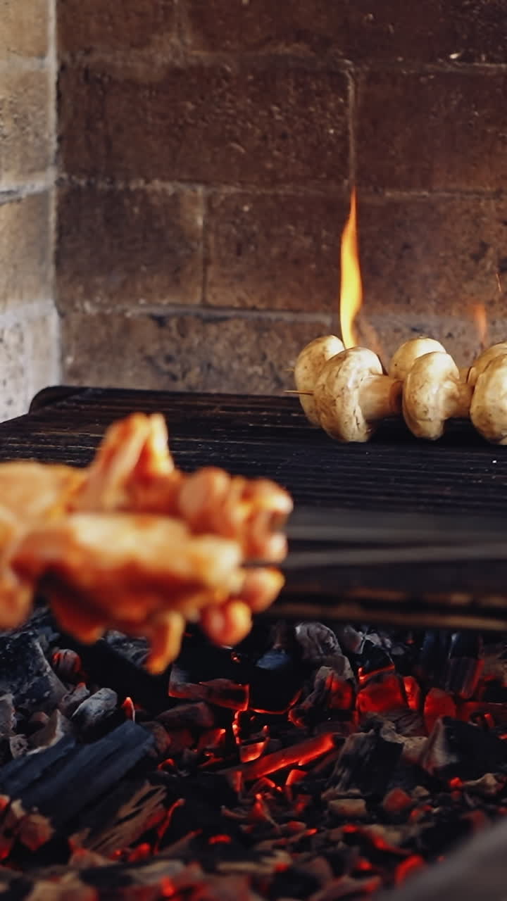 Cooking mushrooms on grill. Cook puts some skewers with chicken meat on charcoal. Preparing the barbeque on the restaurant kitchen. Vertical video