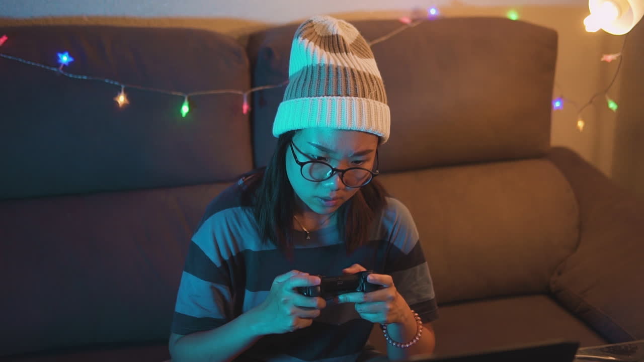 Asian girl wearing glasses gaming at home with a wireless controller