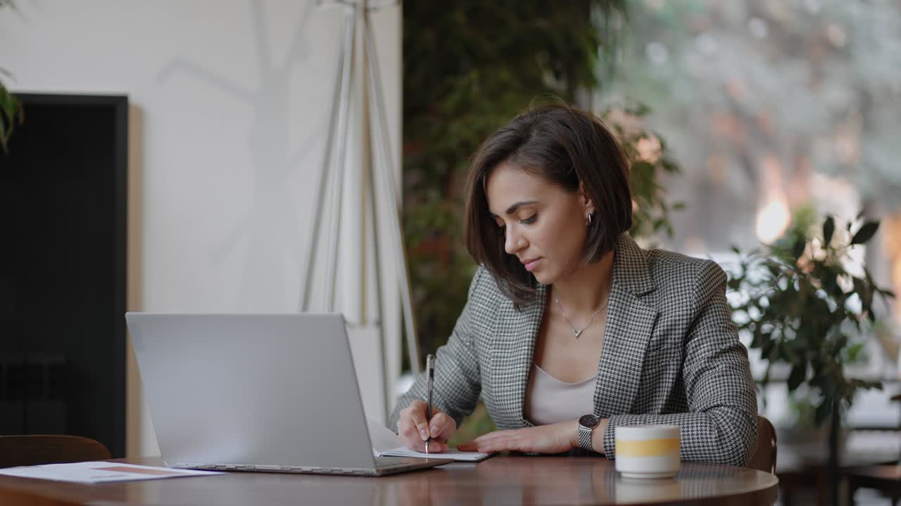 mujer de negocios escribiendo algo en un cuaderno. mujer emprendedora estudiante estudiando escribiendo una nota en el lugar de trabajo cerca de la computadora. una mano de mujer escribiendo en un cuaderno blanco en la mesa.