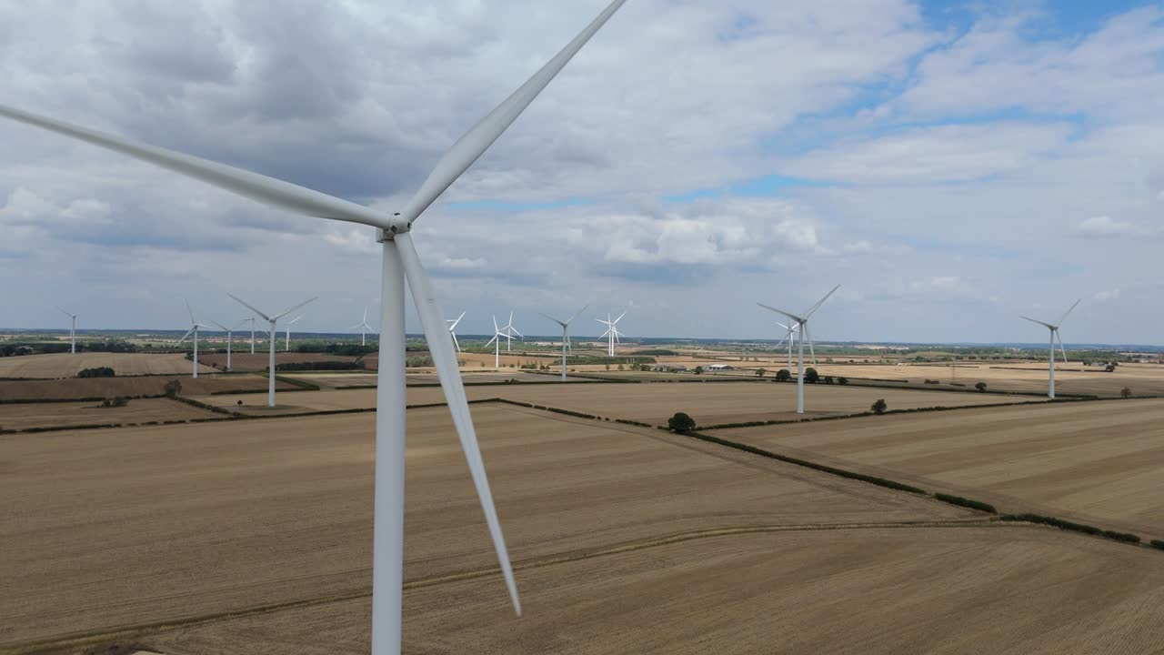 Drone footage of white wind turbines turning above golden fields near Burton Latimer England showing renewable electricity production