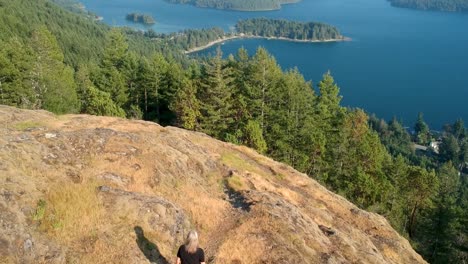 Girl-walking-along-cliff-to-reveal-lake-and-mountains