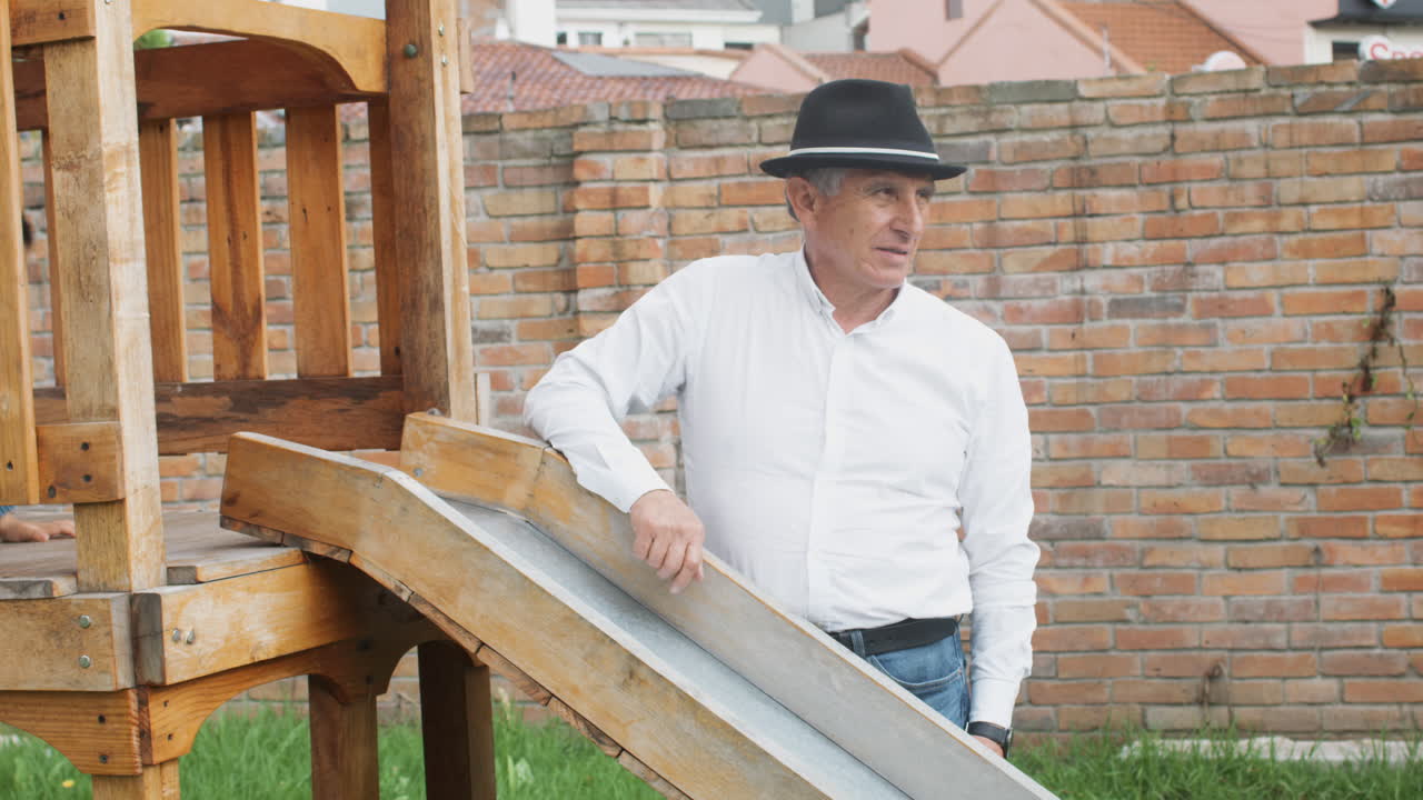 A tender moment between grandfather and grandson as they play together in a wooden playhouse with a slide in the backyard.