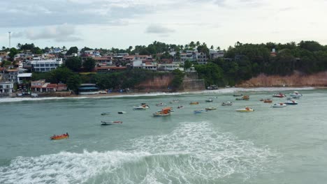 Hermosa-Toma-Aérea-De-Un-Grupo-De-Pequeños-Barcos-De-Pesca-Atracados-En-La-Playa-Tropical-De-Pipa-Durante-La-Marea-Alta-Rodeada-De-Grandes-Acantilados,-Casas-Y-Restaurantes-En-Río-Grande-Do-Norte,-Brasil