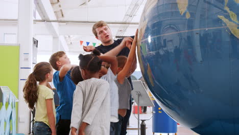 Schulkinder-Benutzen-Riesigen-Globus-Mit-Lehrer-Im-Wissenschaftszentrum