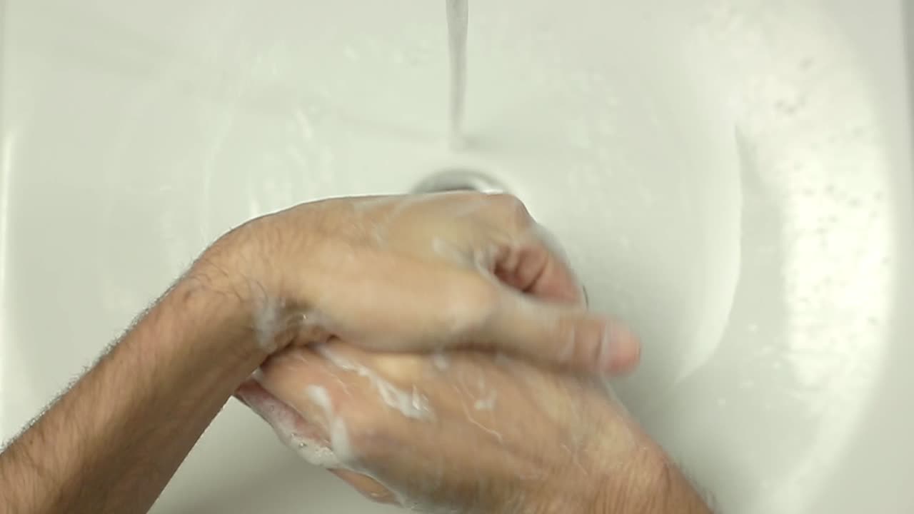 Primo piano di mani che si lavano con acqua e sapone in un lavandino bianco