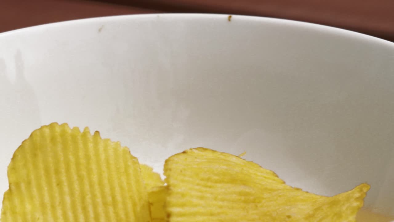 SideView of Crinkle Cut Potato Chips Crisps Falling into White Bowl in Slow Motion - 4K Junk Food Clip