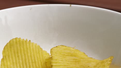 SideView-of-Crinkle-Cut-Potato-Chips-Crisps-Falling-into-White-Bowl-in-Slow-Motion---4K-Junk-Food-Clip