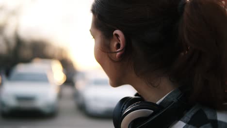 Side-view-of-a-girl-with-headphones-around-her-neck.-She-smiles,-turns-to-look-in-a-blurred-perspective.-Long-brown-haired